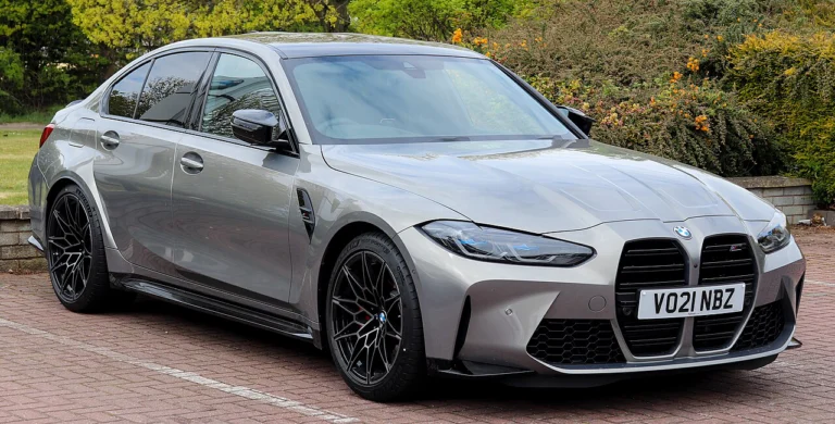Gray BMW M3 Competition sedan parked beside a driveway